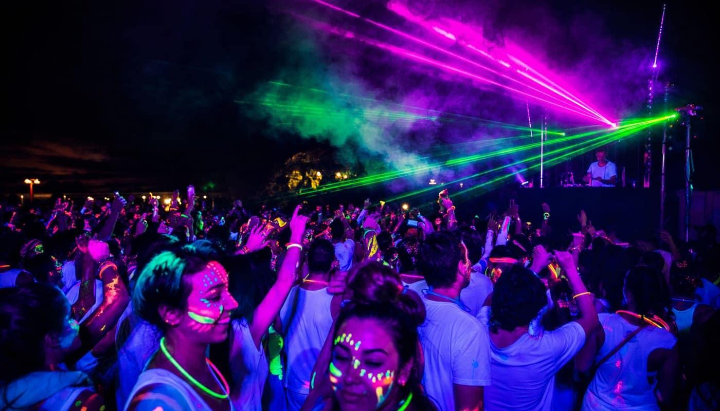 Folla che balla con body paint fluo sotto luci UV e laser a Festichola